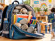 Geöffneter Schulrucksack voller Steine, Schulhefte und Stifte in einem hellen Grundschulraum. Im Hintergrund sind Kinder zu sehen.