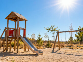 Menschenleerer Spielplatz ohne Sonnenschutz in der glühenden Mittagssonne mit trockener, spärlicher Vegetation. KI-generiertes Bild.