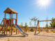 Menschenleerer Spielplatz ohne Sonnenschutz in der glühenden Mittagssonne mit trockener, spärlicher Vegetation. KI-generiertes Bild.